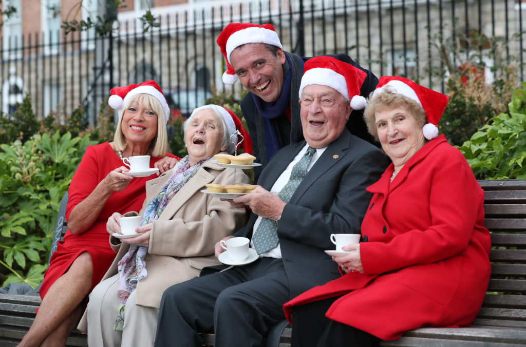 A group of people wearing santa hats sitting on a park bench